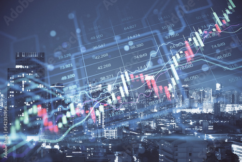 Creative candlestick forex chart index hologram on blurry night city buildings backdrop. Trade, business market and finance analysis concept. Double exposure.