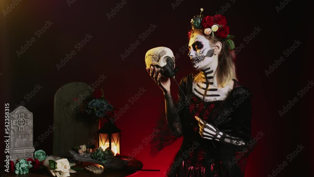 Spooky glamorous woman holding holy skull in studio, acting scary and horror to celebrate mexican halloween day. Flirty goddess wearing festival costume with body art, looking like lady of death. Spooky glamorous woman holding holy skull in studio, acting scary and horror to celebrate mexican halloween day. Flirty goddess wearing festival costume with body art, looking like lady of death.