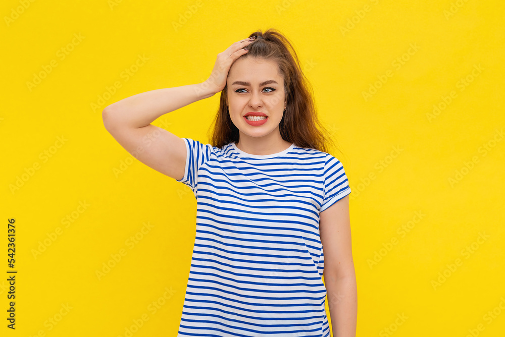 Shocked young woman forgot, remember smth, slap forehead and gasping startled, realize something, standing in white-blue striped t shirt over yellow background