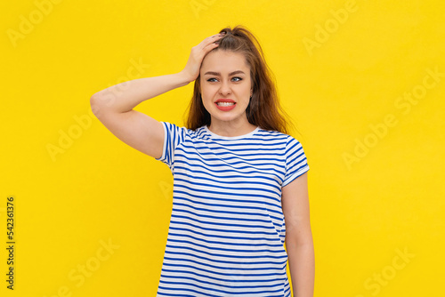 Shocked young woman forgot, remember smth, slap forehead and gasping startled, realize something, standing in white-blue striped t shirt over yellow background