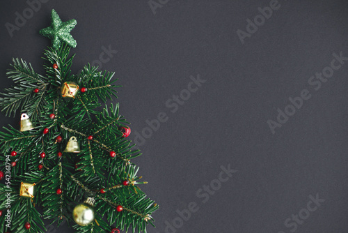 Christmas tree, winter holidays concept. Stylish christmas tree made of fir branches, red berries and gold baubles on black background, flat lay. Creative idea. Modern festive banner