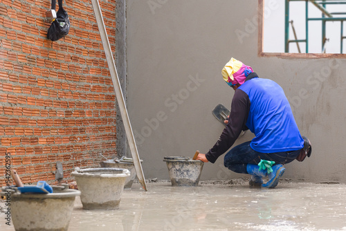 Rear side view of Asian builder using trowel to polishing concrete wall in house construction site