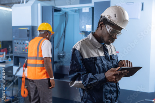Industry worker african holding tablet, background engineer use CNC machine. Concept team work industrial