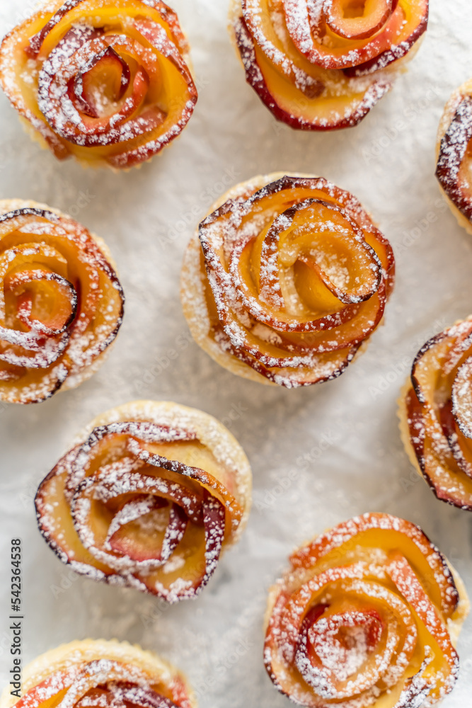 Baked apple pies in form of roses with cinnamon and cloves on a baking pan