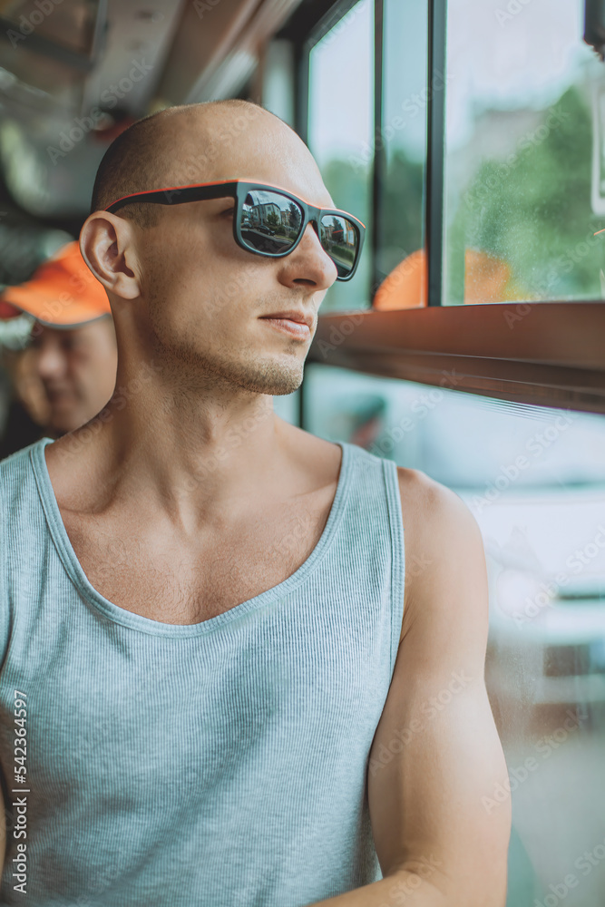 Young mansmartphone travelling by bus in city. A young man wearing a T-shirt and sunglasses uses a mobile phone on public transport. A man on a bus with a mobile phone