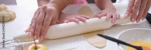 Mom and daughter roll out the dough with rolling pin in kitchen
