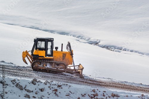 Heavy duty road building machinery bulldozer or earthmover on construction site on snowcovered hill in winter