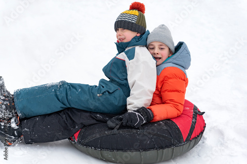 Boys slide down slope on inflatable sled. Children in winter jumpsuits and knitted hats have fun in winter outside. photo