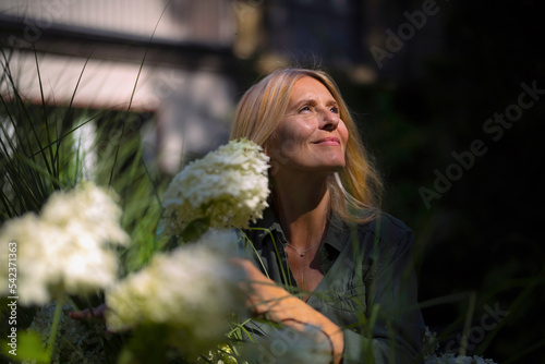 Smiling mature woman standing by flowering plant in garden