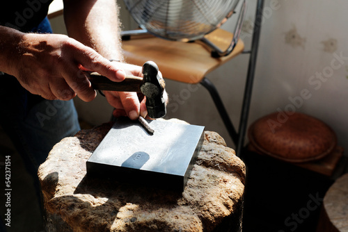 Jeweller hammering on metal to make jewelry in workshop photo