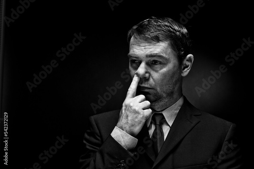 Mature man putting finger in nose against black background photo