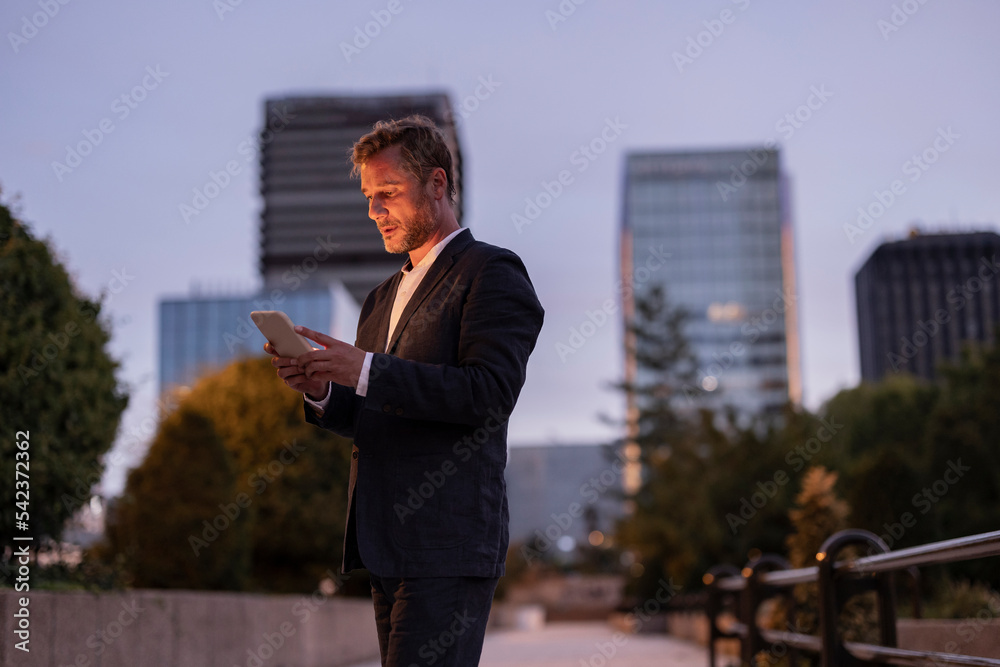 Businessman text messaging on smart phone at footpath Businessman text messaging on smart phone at footpath