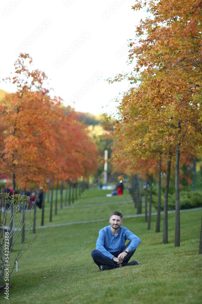 A bearded sportsman sits in the Sofiiv Park in Uman in autumn. All around are bright young maples and a beautiful lawn. A place for recreation outside the city A bearded sportsman sits in the Sofiiv Park in Uman in autumn. All around are bright young maples and a beautiful lawn. A place for recreation outside the city