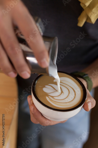 Detail shot of coffee latte being poured to form shapes by a barista out of focus hand. Training barista drawing concept.