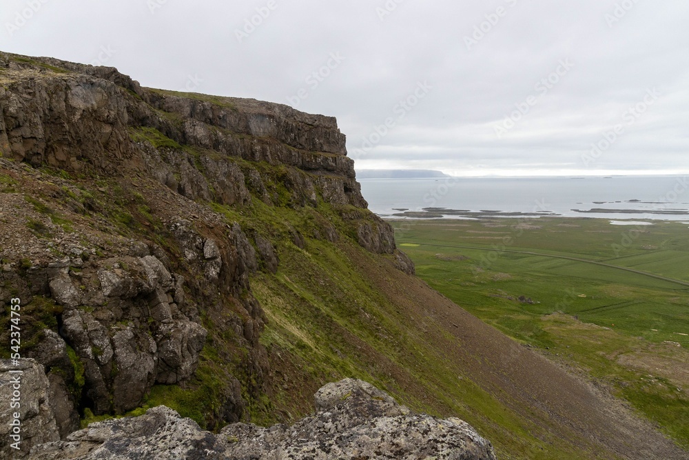 Lovely view of a tall rocky hill overlooking beautiful green hills under an overcast sky in Iceland