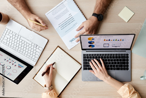 Φωτογραφία Hands of two young analysts or brokers using laptops and making notes while taki
