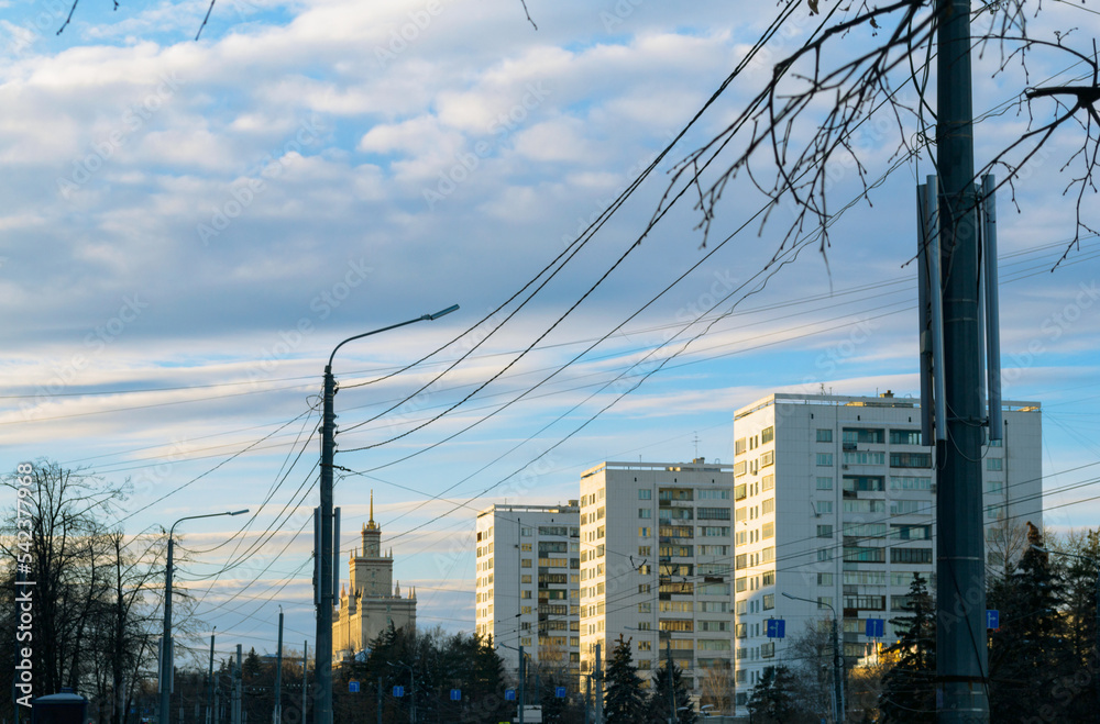 Soviet high-rise residential buildings and the university building are illuminated by the sun. They and lampposts stand in a row on a winter evening