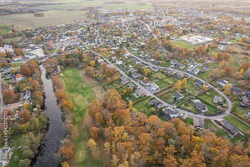 Aerial view on a little village in Europe, private houses. Multicolored trees in autumn, and green grass, forest, wild nature, river, contrasts. Cozy atmosphere. 