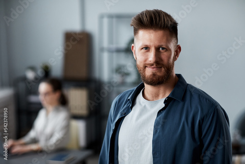 Young successful chief executive officer or manager in casualwear looking at camera while standing against his colleague in office © Seventyfour