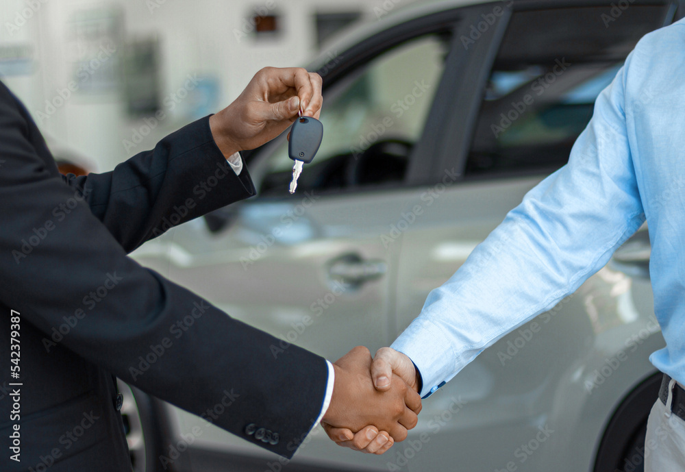 Close up of consultant giving car key to buyer after successful deal in auto show Close up of consultant giving car key to buyer after successful deal in auto show