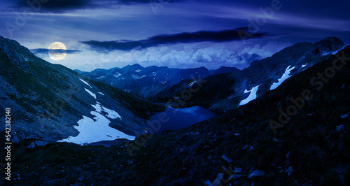 panoramic view of a lake in fagaras mountains at night. summer landscape on in full moon light. travel season in romania