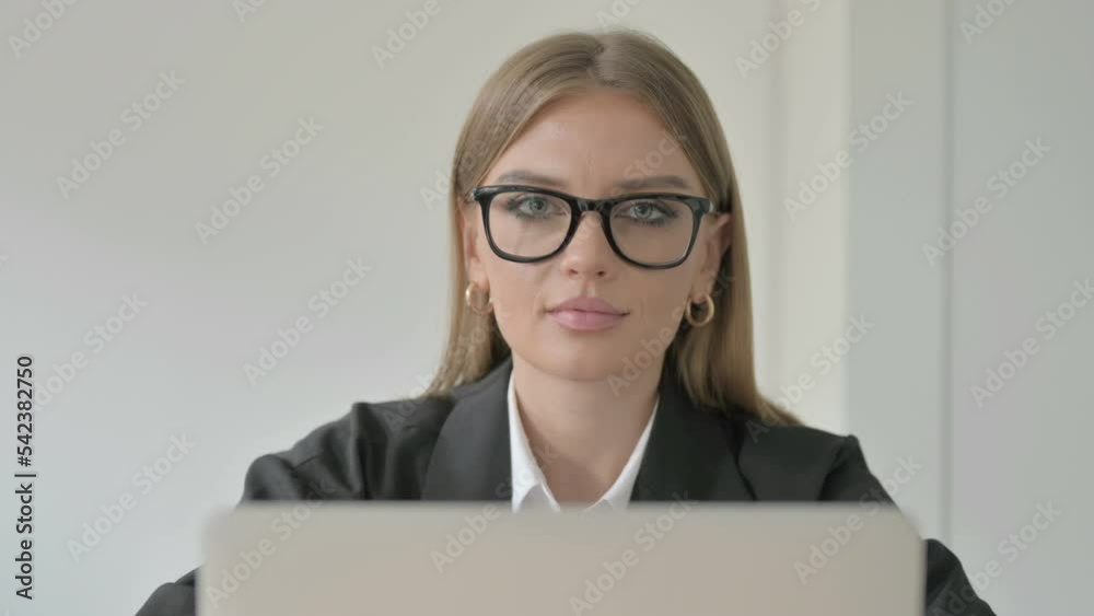 Close Up of Young Businesswoman Looking at Camera while using Laptop Close Up of Young Businesswoman Looking at Camera while using Laptop