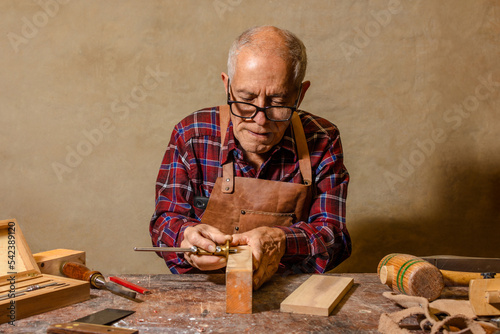 Old latin carpenter with gray hair using a gauge to mark a piece of wood on a table full of tools photo