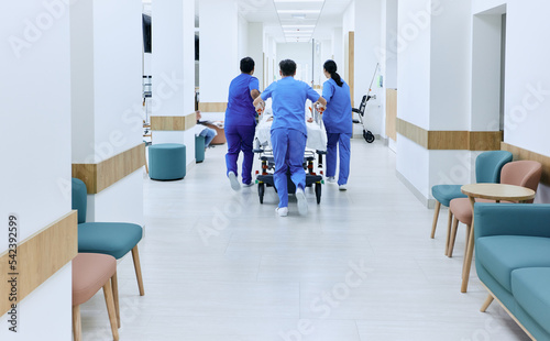 Hospital care team hastily wheeling patient on medical gurney at emergency department of hospital, back view. Work of emergency medical team photo