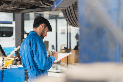 Auto check up and car service shop concept. Mechanic writing job checklist to clipboard to estimate repair quotation to client at workshop garage.