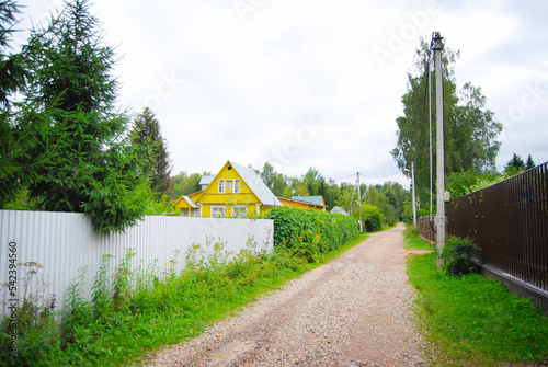 A simple rural dirt road in Russia. The road in the country village. Rustic landscape. The road in the village. Country village. Wooden houses. Rural landscape. Summer in the country.