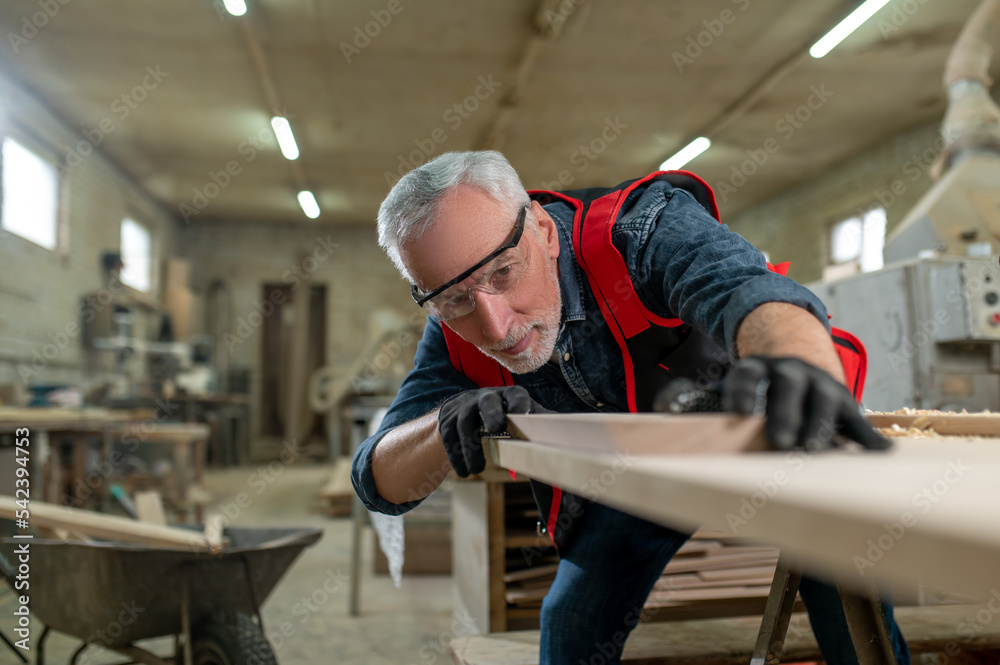 Carpenter in protective galsses working with wood and looking concentrated Carpenter in protective galsses working with wood and looking concentrated