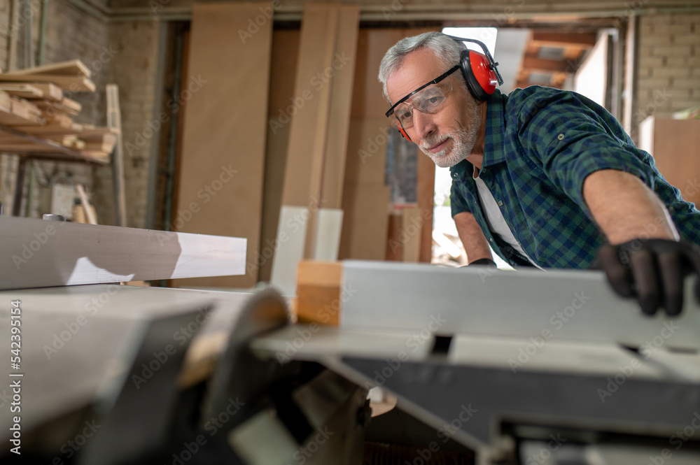 Carpenter in ear protectors working in a workshop Carpenter in ear protectors working in a workshop