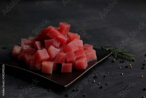 Raw fresh Tuna cube on black plate. Black wooden background.