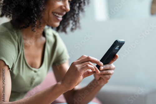 Shot of confident woman using her mobile phone while drinking coffee sitting on sofa at home.