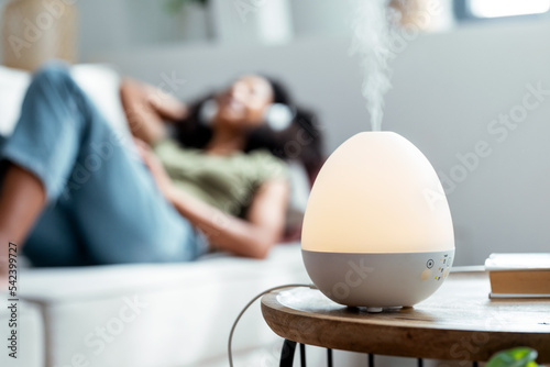 Essential oil aroma diffuser humidifier diffusing water articles in the air while woman listening music lying on coach. photo