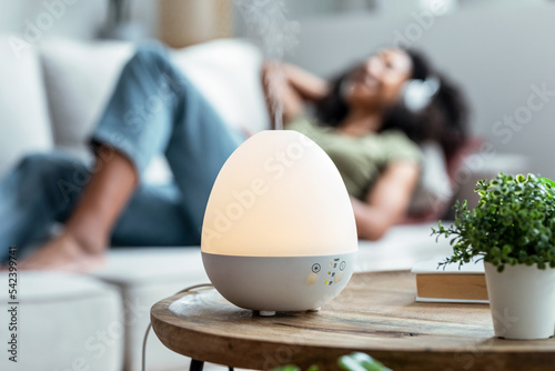 Essential oil aroma diffuser humidifier diffusing water articles in the air while woman listening music lying on coach. photo