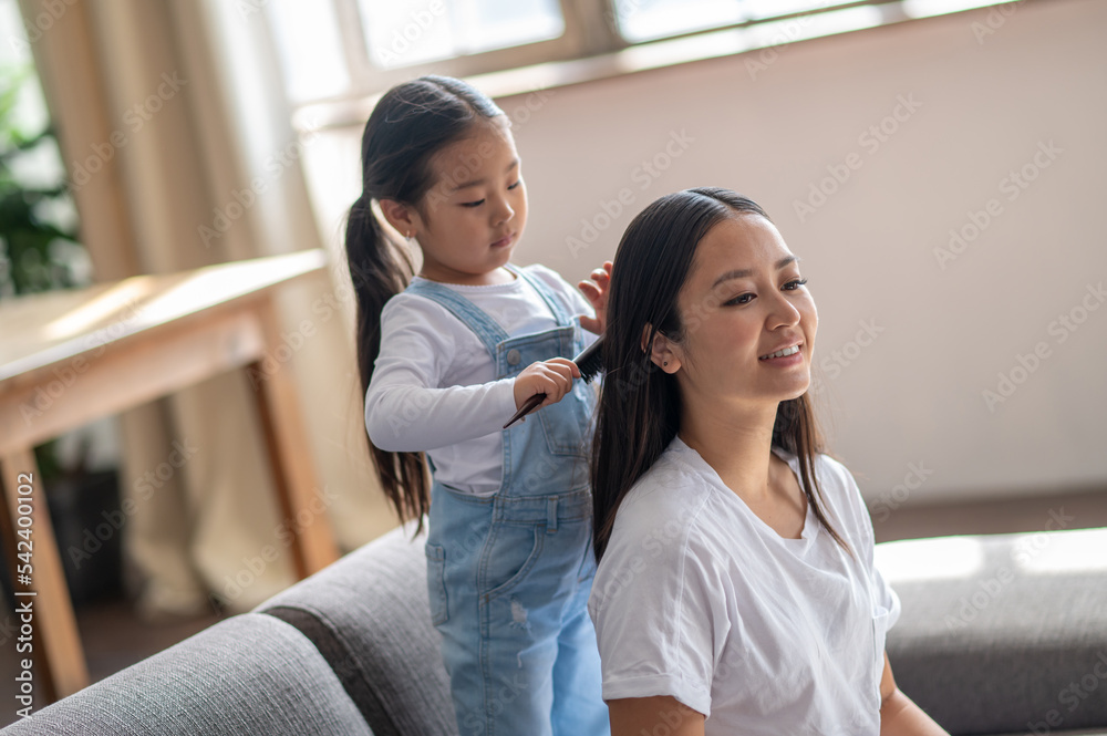 Fototapeta premium Caring child combing her mother hair with a hairbrush s