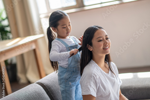 Caring child combing her mother hair with a hairbrush s