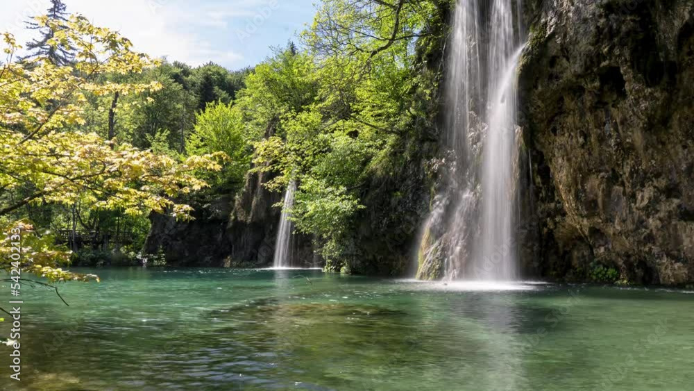 A beautiful waterfall falls onto a green lake, static wide shot A beautiful waterfall falls onto a green lake, static wide shot
