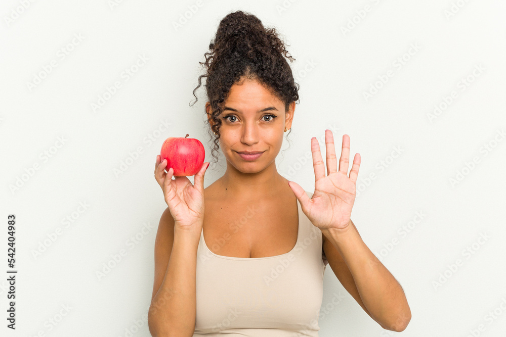 Young brazilian woman holding a red apple isolated smiling cheerful showing number five with fingers. Young brazilian woman holding a red apple isolated smiling cheerful showing number five with fingers.