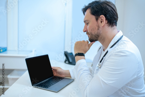 Dark-haired bearded young doctor at his working place in the hospital
