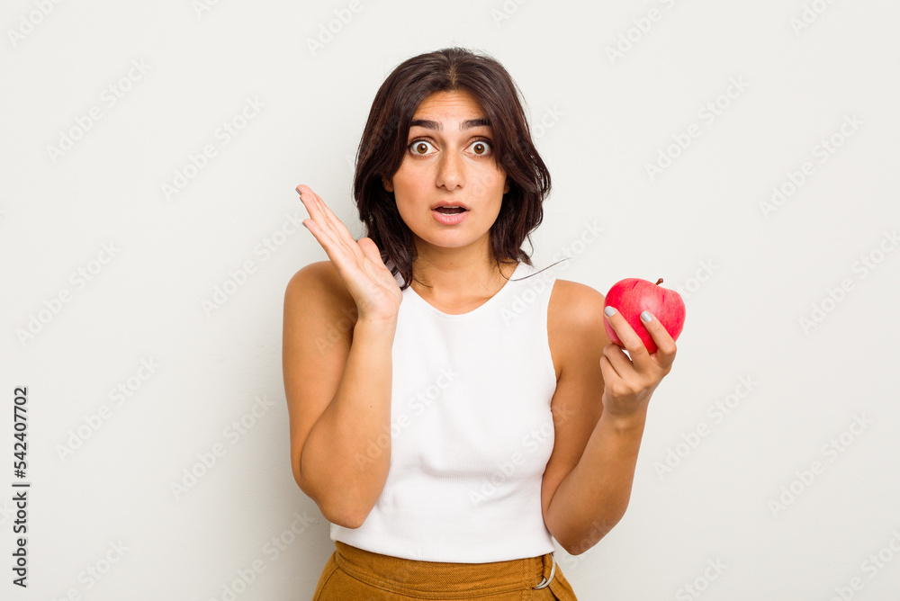 Young Indian woman holding an apple isolated on white background surprised and shocked. Young Indian woman holding an apple isolated on white background surprised and shocked.