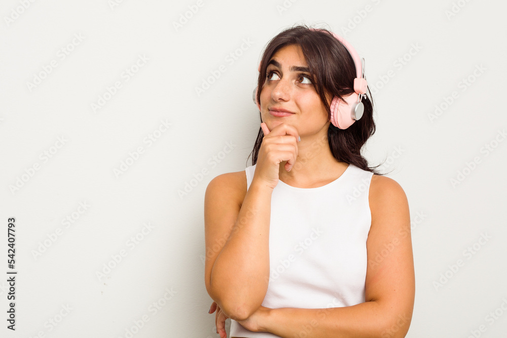 Young Indian woman wearing headphones isolated on white background looking sideways with doubtful and skeptical expression. Young Indian woman wearing headphones isolated on white background looking sideways with doubtful and skeptical expression.