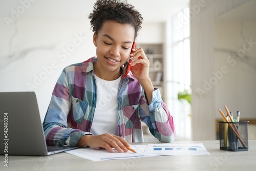 Mixed race teen girl school student call by phone, discussing homework with friend, sitting at desk photo