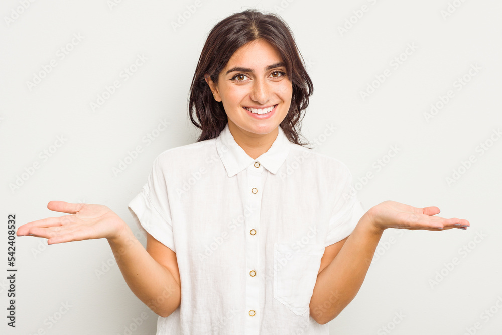 Young Indian woman isolated on white background makes scale with arms, feels happy and confident. Young Indian woman isolated on white background makes scale with arms, feels happy and confident.