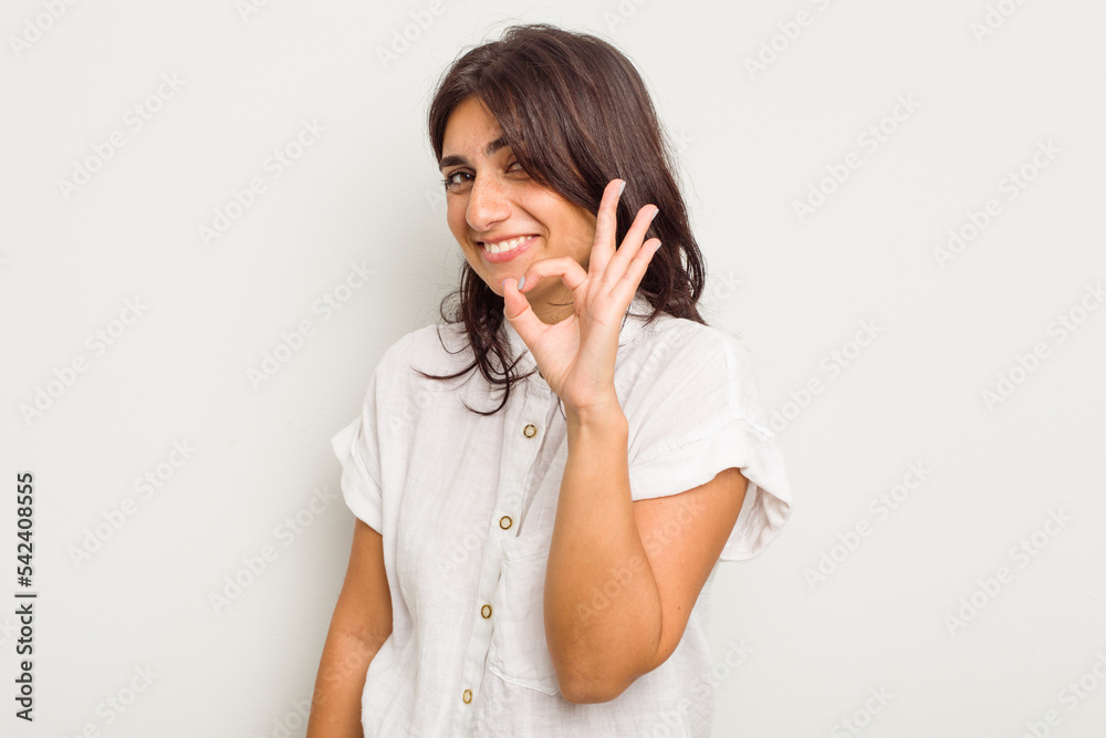 Young Indian woman isolated on white background winks an eye and holds an okay gesture with hand. Young Indian woman isolated on white background winks an eye and holds an okay gesture with hand.