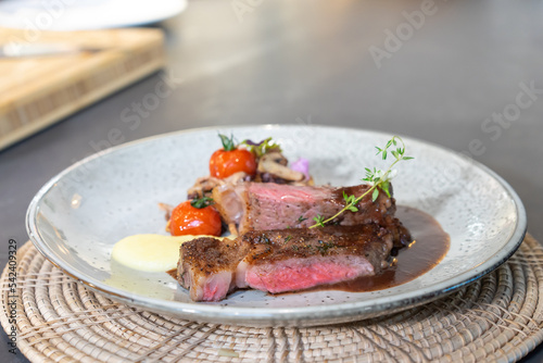 Medium Rare Beef Steak was grilled and fried with sliced mushroom and mini tomato on white dish, ready to serve and eat.