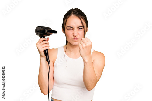 Young caucasian woman holding a hairdryer on green chroma background showing fist to camera, aggressive facial expression.