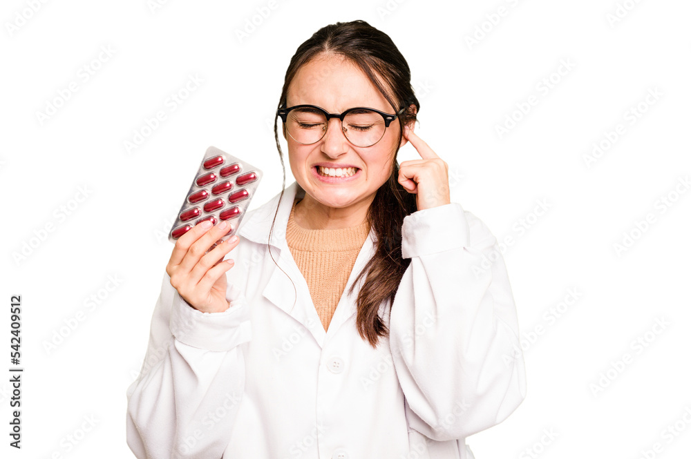 Young pharmacist woman holding a pills isolated on green chroma background covering ears with hands. Young pharmacist woman holding a pills isolated on green chroma background covering ears with hands.