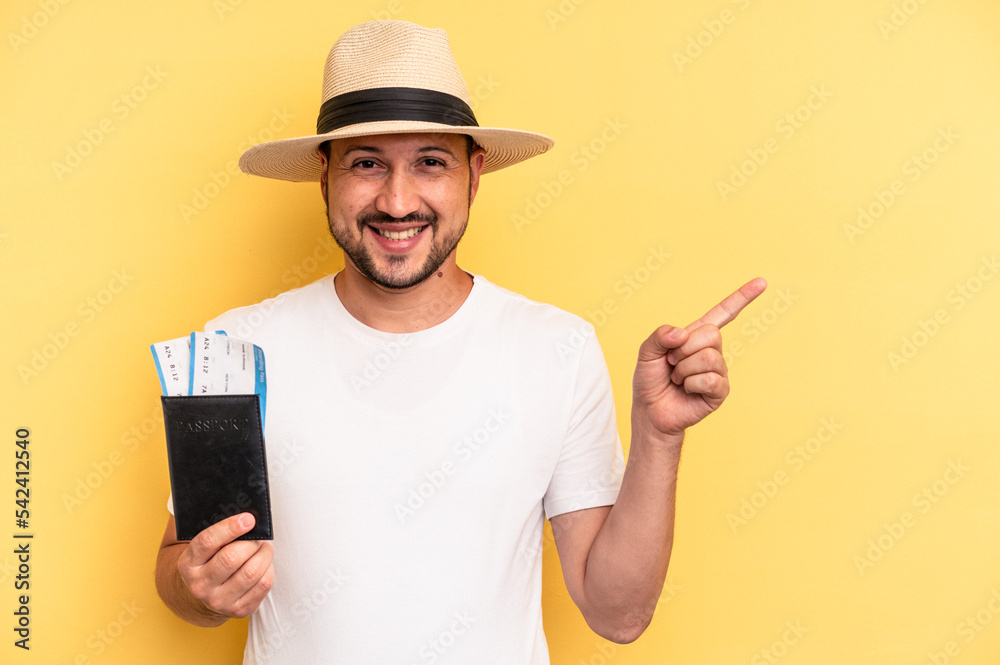 Young latin man holding a flight tickets for vacations smiling and pointing aside, showing something at blank space.
